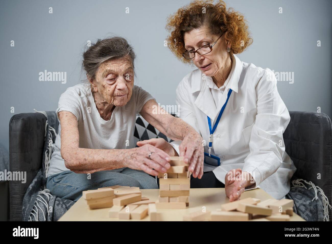 Jenga-Spiel. Thema sind Demenz, Altern und Spiele für alte Menschen. Kaukasische ältere Frau baut mit dem Hel einen Turm aus Holzblöcken Stockfoto