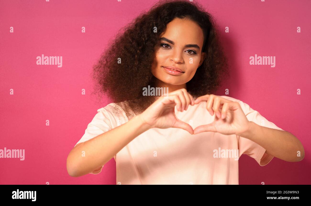 Liebe Geste mit einem zarten Blick schöne junge afroamerikanische Frau, die positiv auf die Kamera in peachy T-Shirt isola Stockfoto