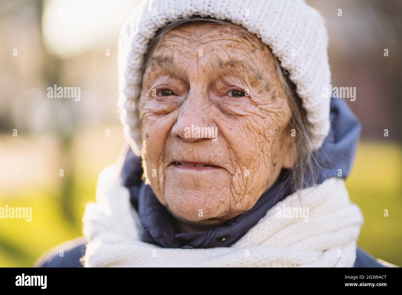 Porträt kaukasische ältere Frau mit grauen Haaren und tiefen Falten 90 Jahre alt posiert in warmer Kleidung, weiß gestrickter Schal und ha Stockfoto
