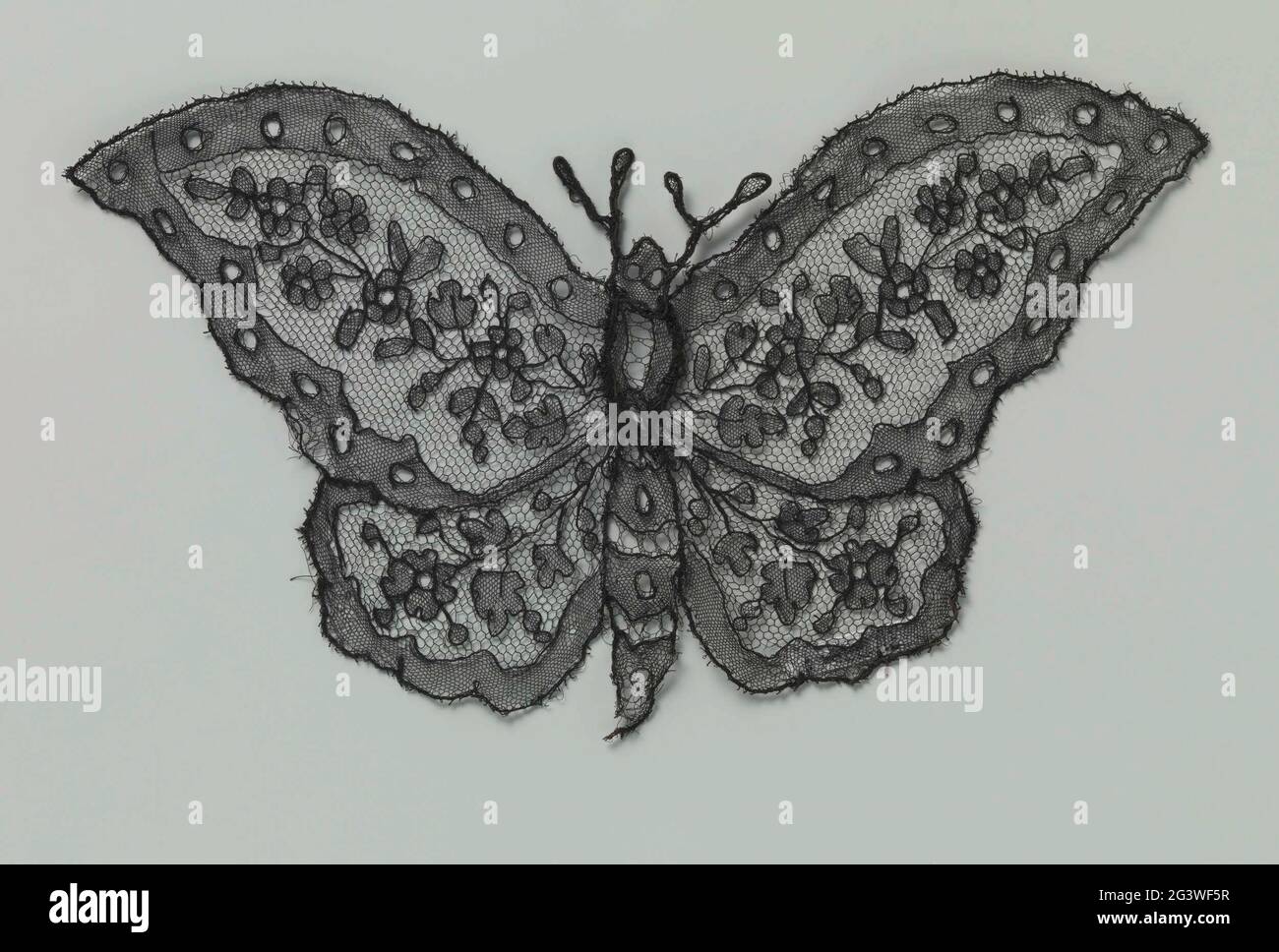 Anwendung der Spannseite in Form eines Schmetterlings. Anwendung in Form eines blacklock-Seitenschmetterlings: Chantilly-Seite. Das Muster in jedem der vier Flügel besteht aus einem Zweig mit einer oder mehreren Rosettenblüten und -Blättern. Die Motive sind durch einen feinen Maas-Boden, einen Tüll, verbunden. Die Motive sind in einer Powerbase mit dickeren Konturdrähten gefertigt. Entlang des Umfangs des Schmetterlings wurde eine breite Kante zu einem Slipbar gemacht, mit ovalen Aussparungen entlang der oberen Flügel. Im Mieder wurde ein dekorativer Boden in breiten und Längsstreifen aufgetragen, ein Rosenboden. Metalldraht ist uns Stockfoto