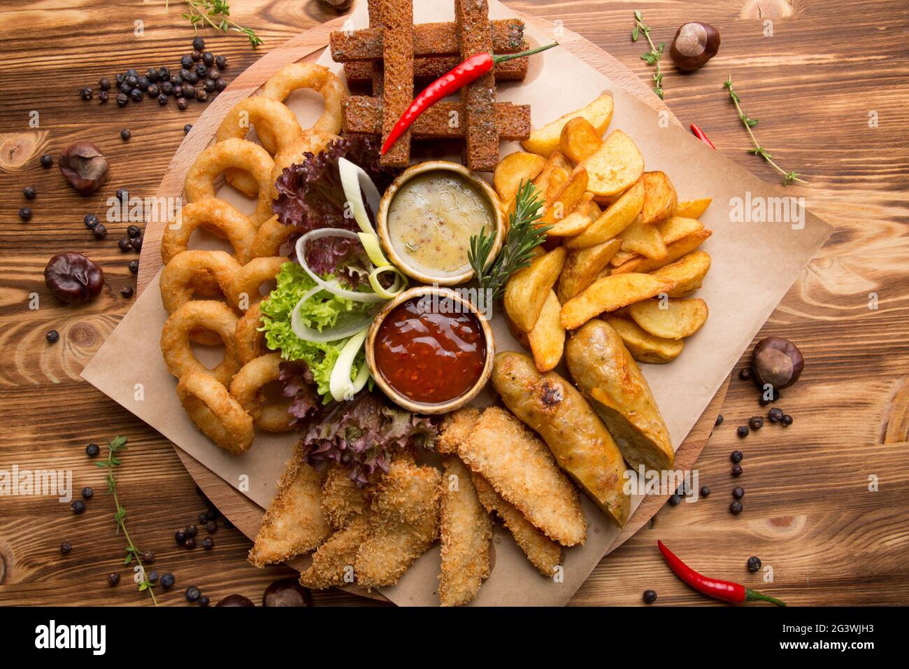 Gebratener Snack für Bier. Großer Teller mit Biersnacks: Croutons, gebratene Zwiebelringe im Teig, pommes Frites, Kartoffelkeile. Heiße Sauce Stockfoto