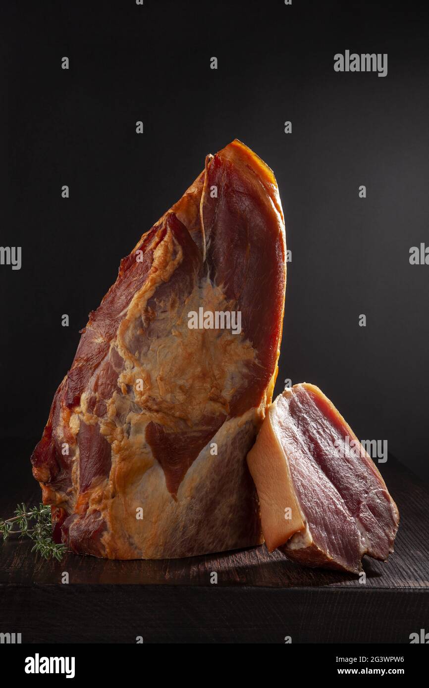 Geräuchertes Fleisch auf schwarzem Hintergrund mit frischen aromatischen Kräutern. Stockfoto