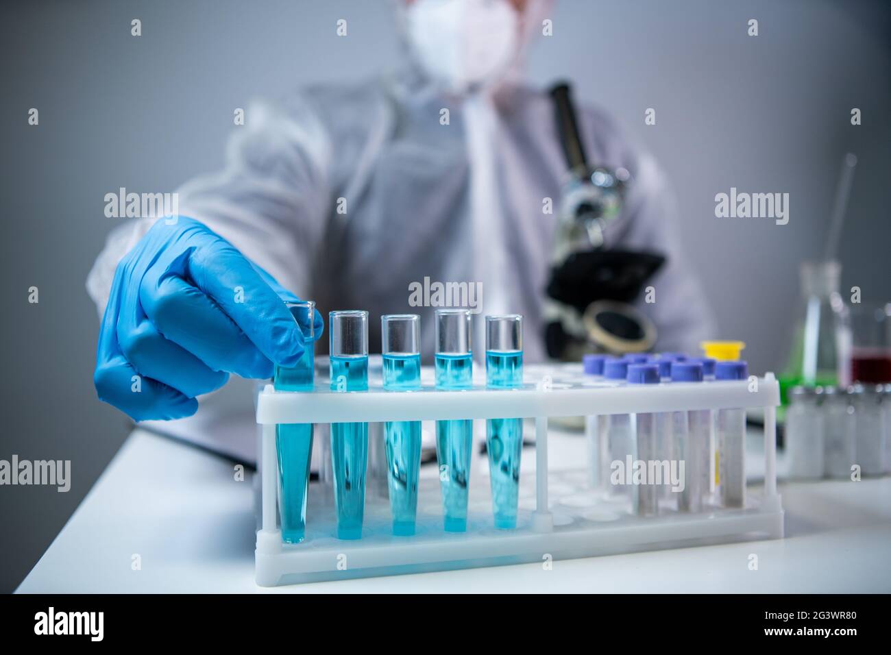 Biochemie Laborforschung, Chemiker im Schutzanzug Analyse blaue Probe im Labor mit Geräten, Mikroskop und Stockfoto