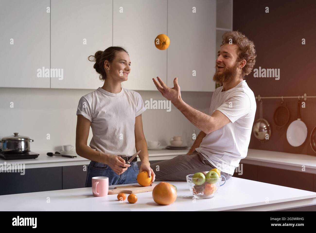 Spielen mit orange jungen Mann glücklich über ihr neues Zuhause junges Paar Kochen in der neuen Küche. Schönes junges Paar im Gespräch enjoyi Stockfoto