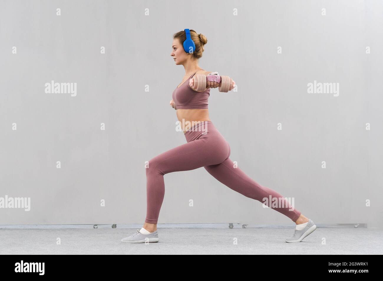 Mädchen in einem engen rosa Outfit Heben Hanteln in einer Kriegerposition. Mädchen verlieren dabei Sport-Übungen Gewichtheben hören Stockfoto