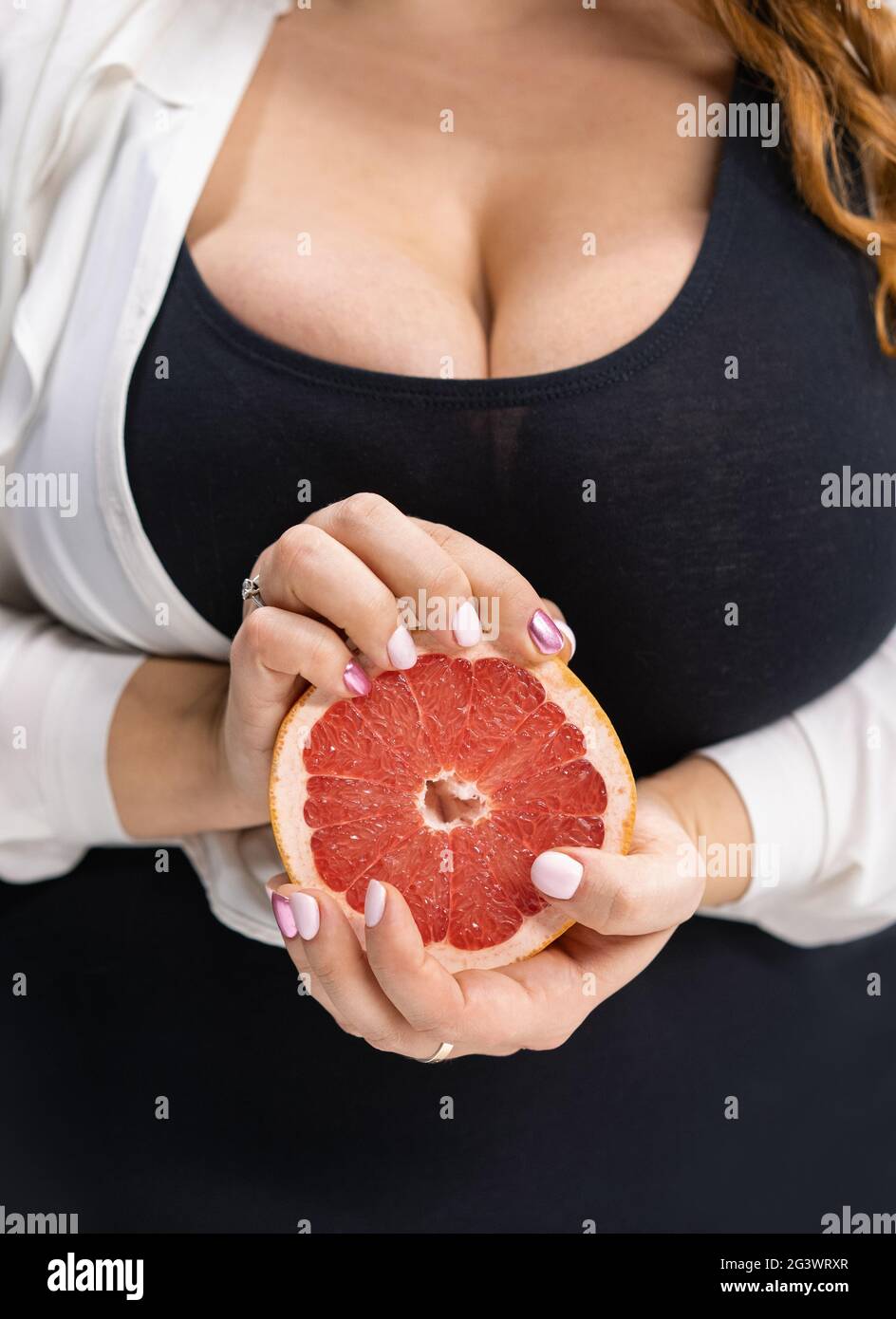 Body positive Mädchen hält eine geschnittene Hälfte einer frischen Grapefruit in den Händen stehen auf der modernen Küche zu Hause mit langen blonden Haaren Stockfoto