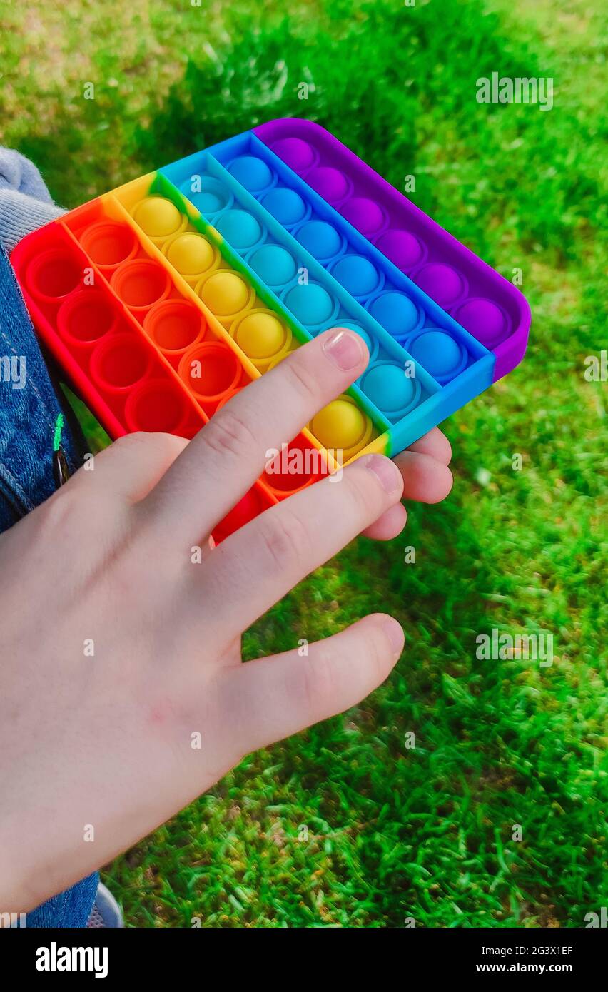 Trendiges entspannendes Spielzeug Pop-it in die Hände des Jungen. Ein Kind hält Anti-Stress-Fidget-Spielzeug popit. Beliebtes Spiel für Erwachsene und Kinder. Hochwertige Fotos Stockfoto