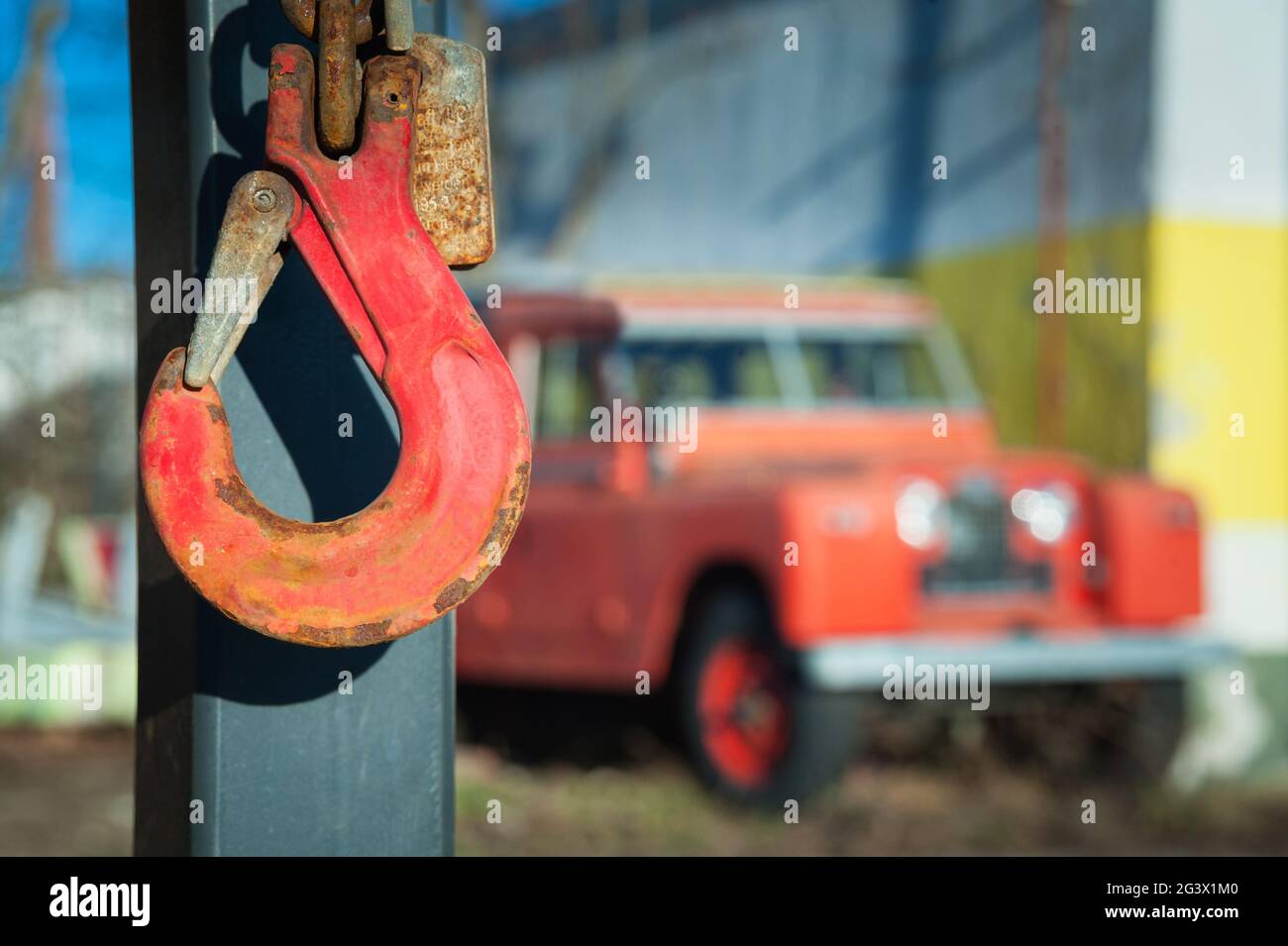 Roter Kranhaken mit Oldtimer Offroad Fahrzeug im verschwommenen Rücken Stockfoto