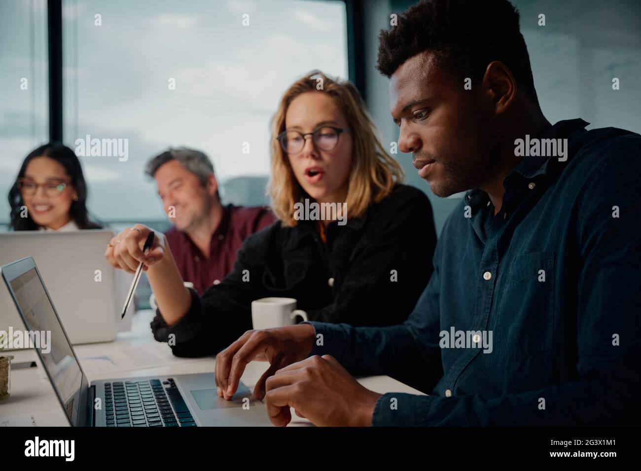 Verschiedene Kollegen aus dem Unternehmen, die während eines Meetings im Büro einen Laptop verwenden Stockfoto