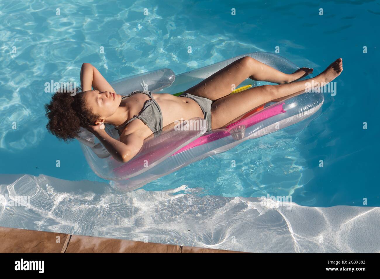Mixed Race Frau Sonnenbaden auf aufblasbaren im Schwimmbad Stockfoto