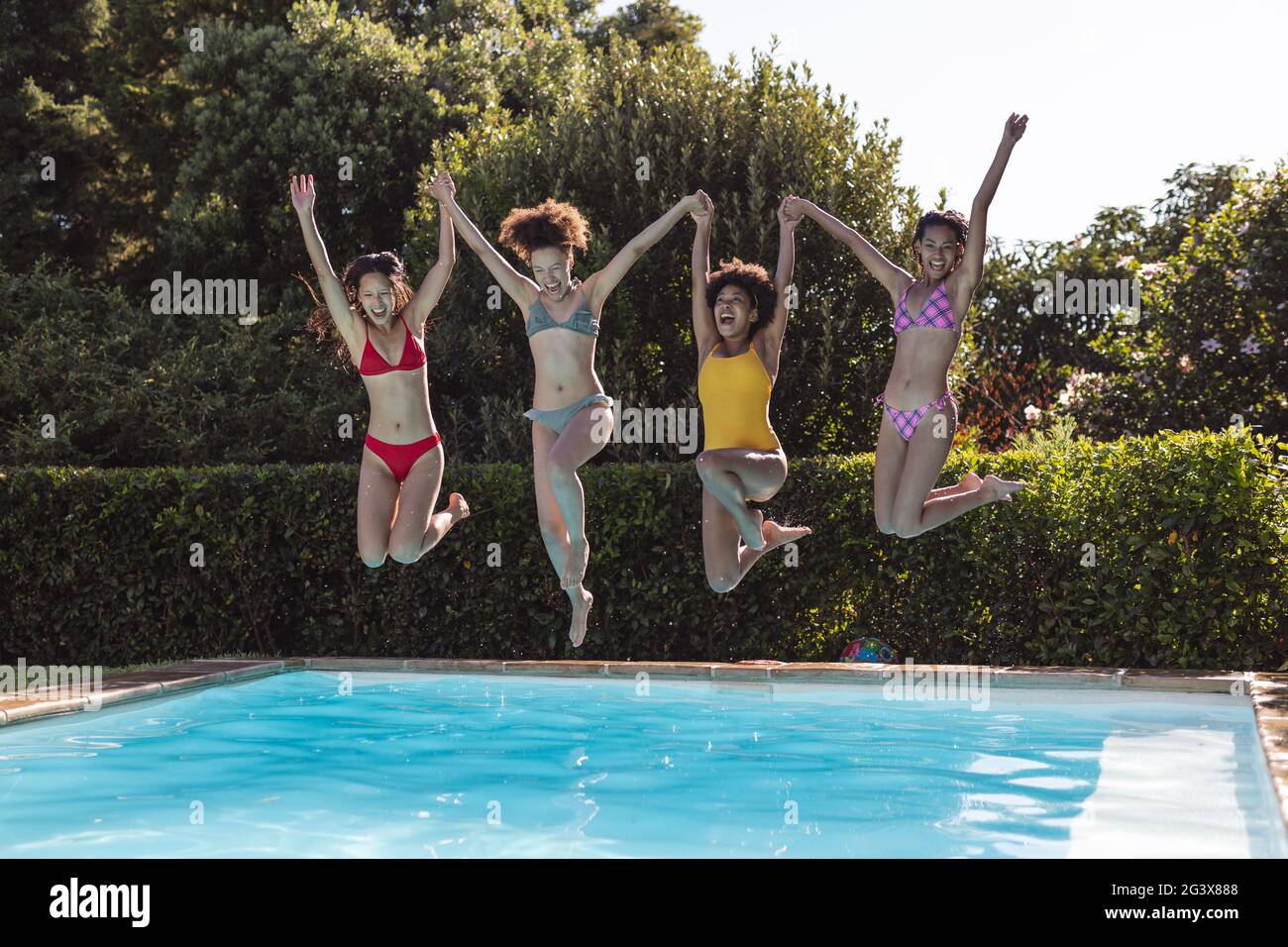 Eine vielfältige Gruppe von Freundinnen, die Spaß haben und bei einer Poolparty ins Wasser springen Stockfoto