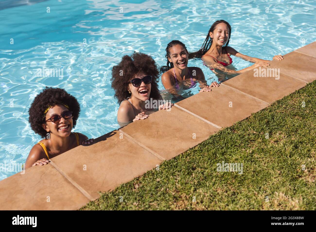 Eine Gruppe von Freundinnen, die am Pool lächelten und sich lehnten Stockfoto