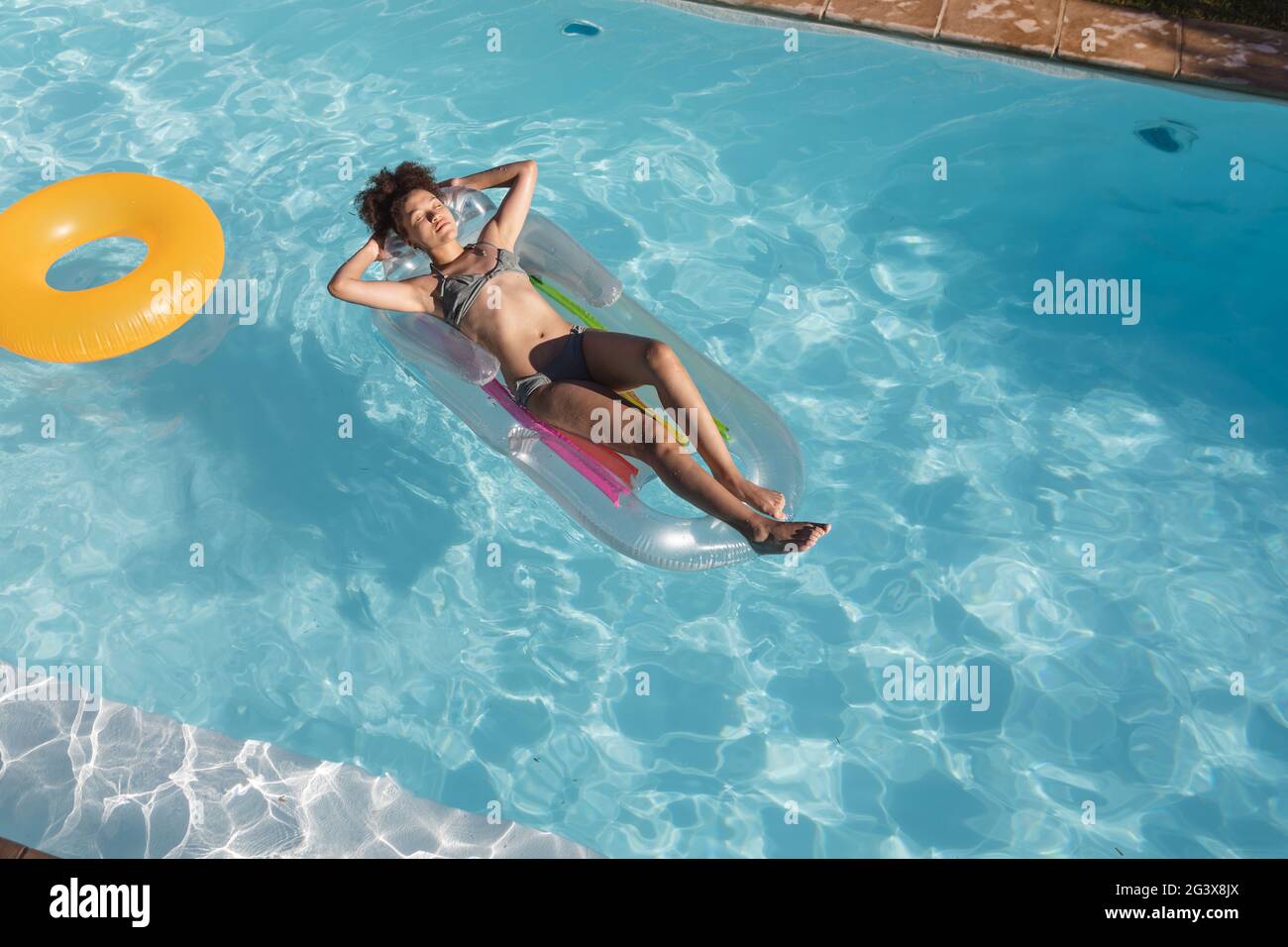 Mixed Race Frau Sonnenbaden auf aufblasbaren im Schwimmbad Stockfoto