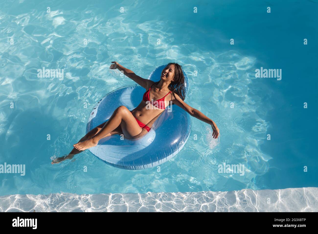 Mixed-Race-Frau, die Spaß beim Spielen auf aufblasbaren und lächelt im Schwimmbad Stockfoto