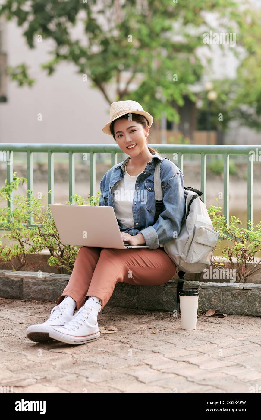 Glückliche junge Reisende Frau mit Rucksack sitzt in der Stadt Eingabe auf ihrem Laptop, Konzept der Technologie, Jugend und digitale Nomaden Lifestyle, Kopie spc Stockfoto