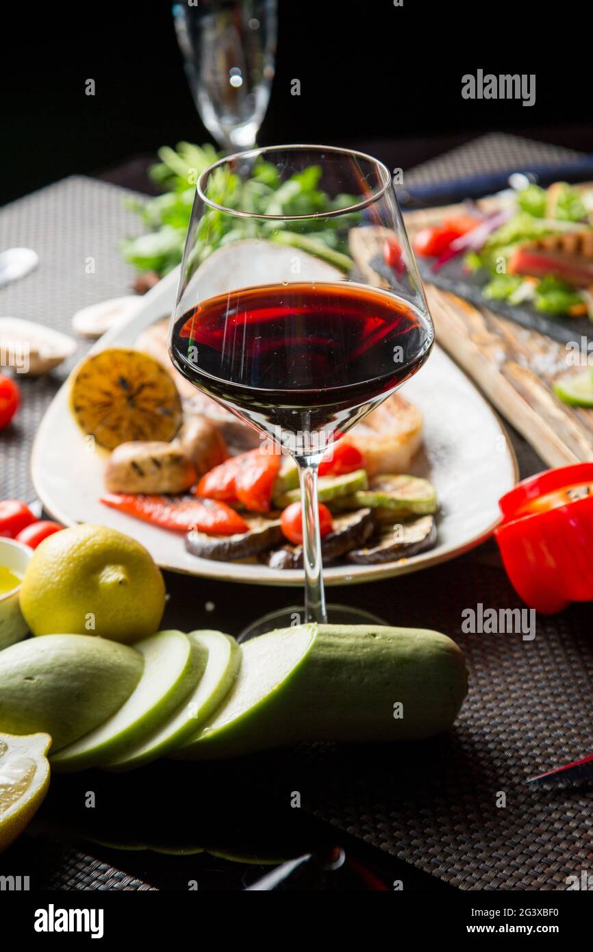 Ein Glas trockener Rotwein, ein Aperitif. Wein mit gegrilltem Fleisch und Gemüse. Nahaufnahme. Konzept - Tischeinstellung in einem Restaurant. Stockfoto