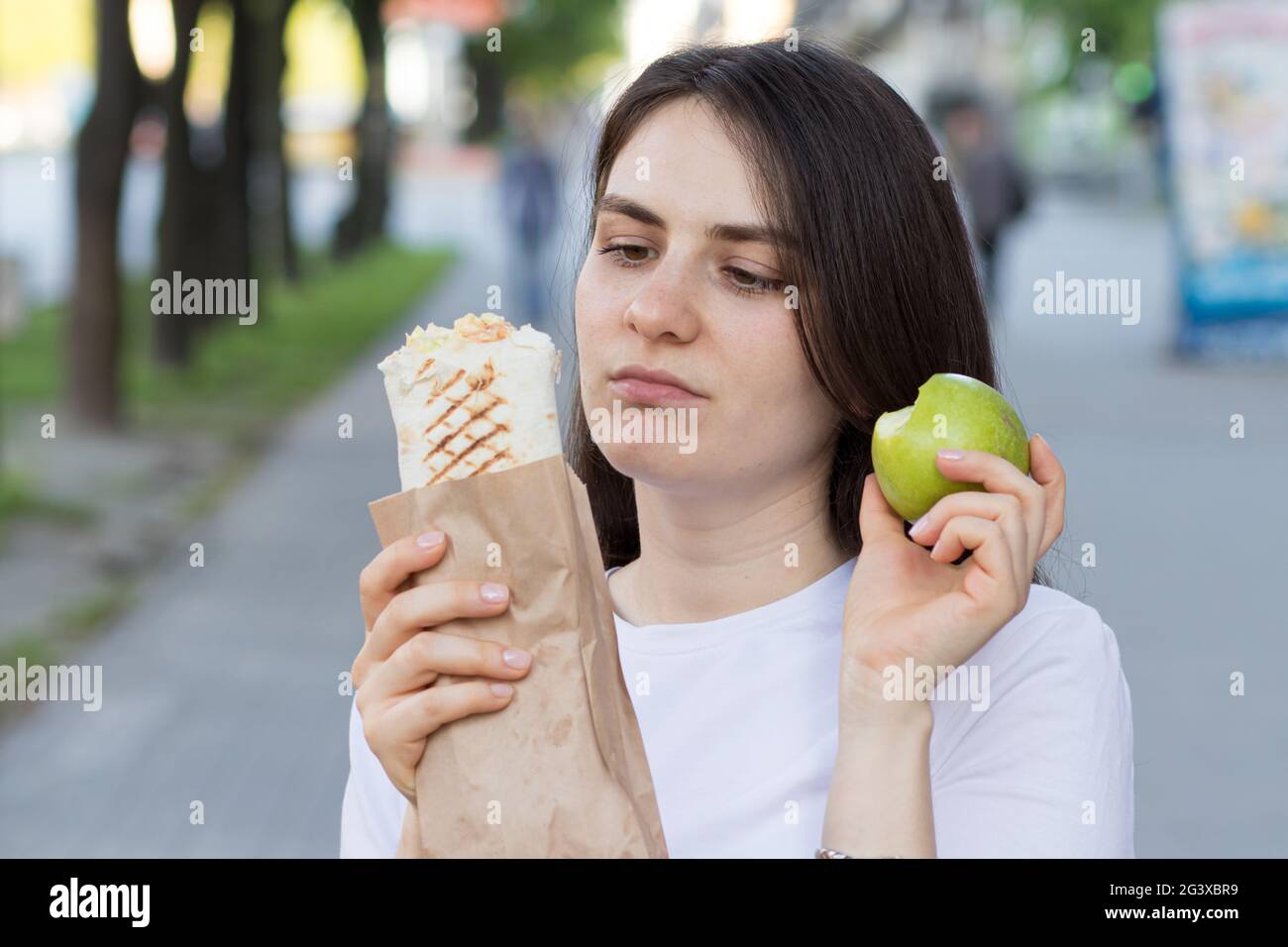 Junge schöne Brünette Frau auf einer Diät wählt Nahrung - was einen Apfel oder Fast Food zu essen. Stockfoto