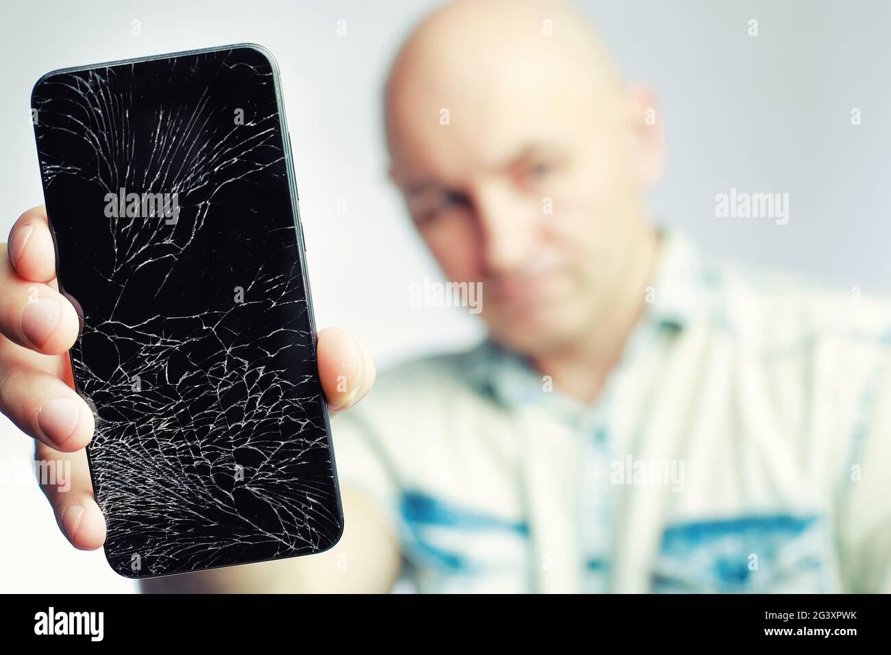 Telefon mit EINEM defekten Bildschirm Nahaufnahme. Ein weißer Mann hält ein schwarzes Smartphone mit einem geknackten Display. Stockfoto