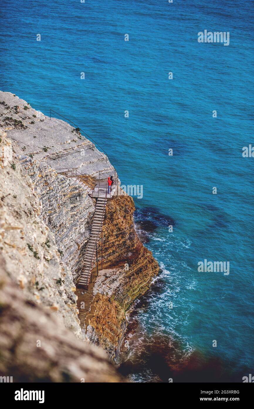 Zwei menschliche Figuren auf leeren Felsen am Meer. Blaues, wunderschönes Meer neben malerischen Klippen im frühen Frühjahr. Konzept - eine Reise Stockfoto