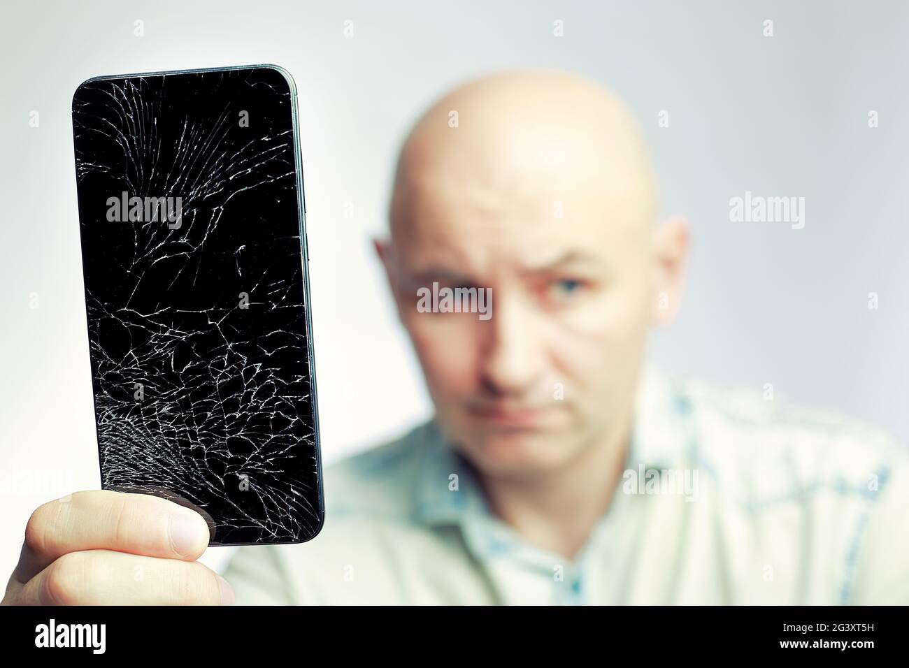 Telefon mit EINEM defekten Bildschirm Nahaufnahme. Ein weißer Mann hält ein schwarzes Smartphone mit einem geknackten Display. Stockfoto