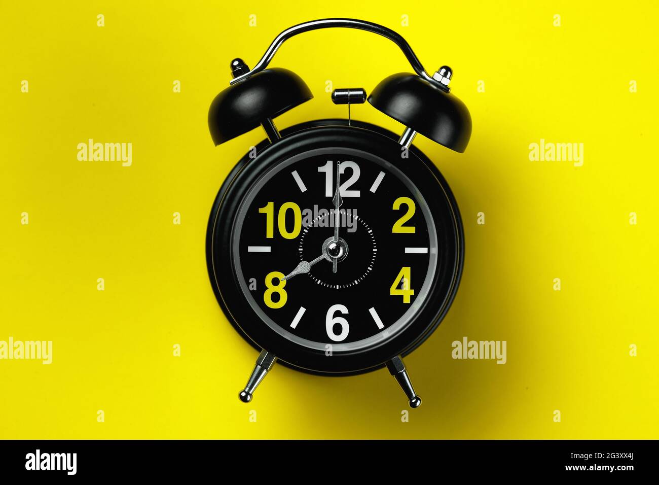 Ein schwarzer runder Wecker liegt auf einem gelben Hintergrund. Acht Uhr vor Mittag Stockfoto