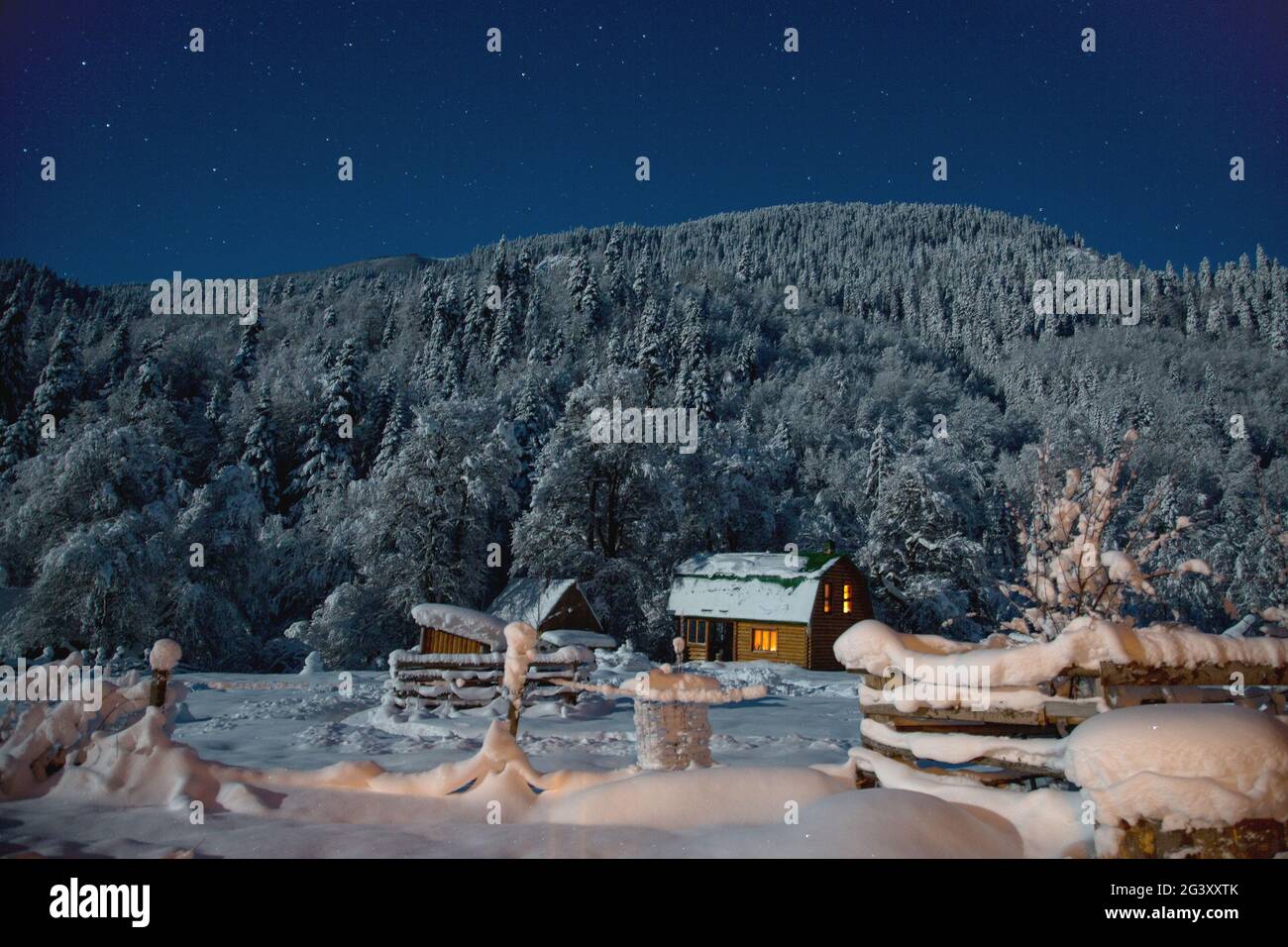 Kleines Haus in einer Winternacht mit glühenden Fenstern im Camping in den Bergen. Kleines Dorf in den Kaukasusbergen. Weihnachtsurlaub Stockfoto