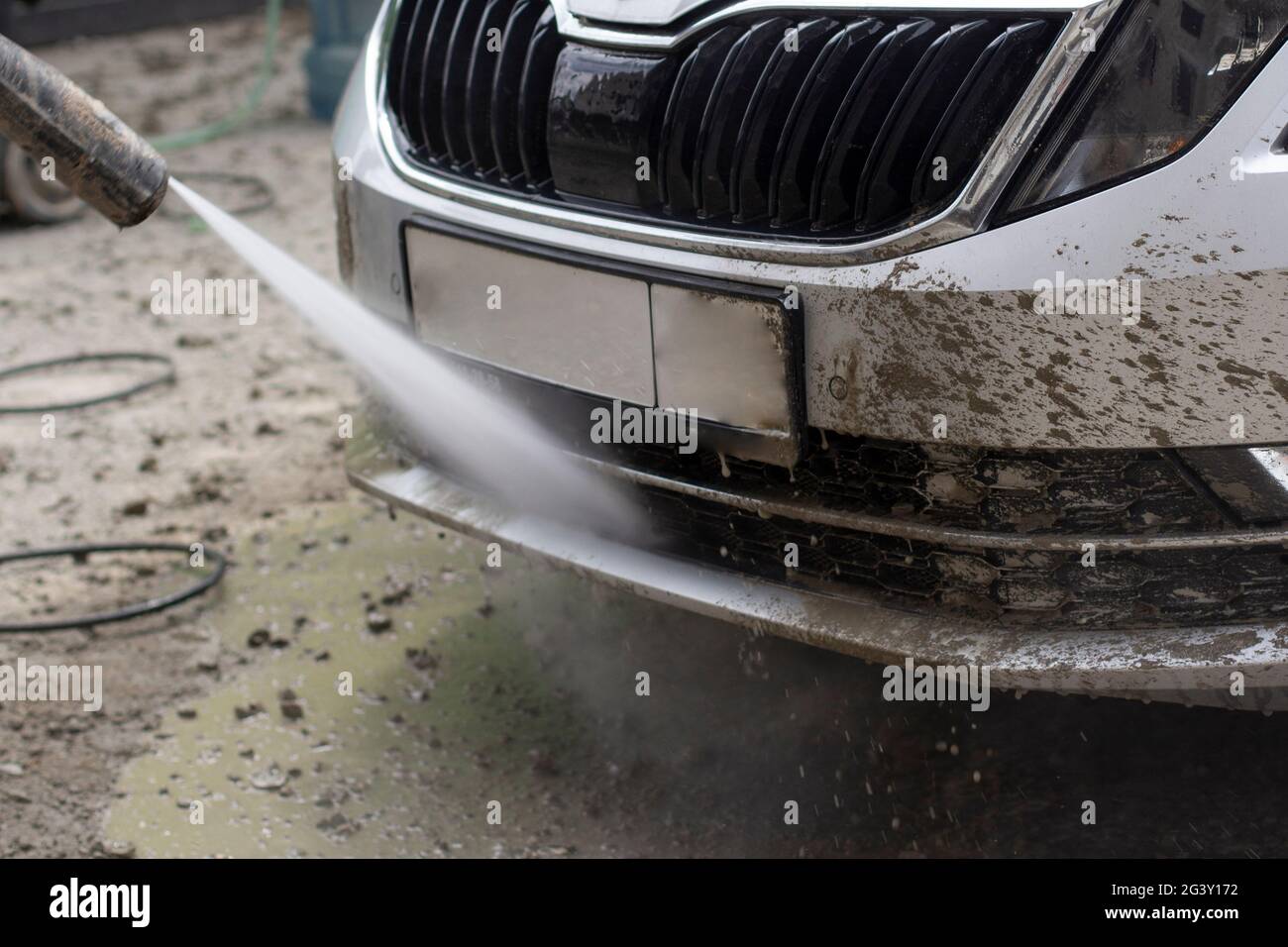 Autowäsche. Das Auto wird unter dem Druck eines Wasserstrahls gewaschen. Mit einem Wasserspray Schmutz von der Fahrzeugoberfläche abwaschen. Stockfoto