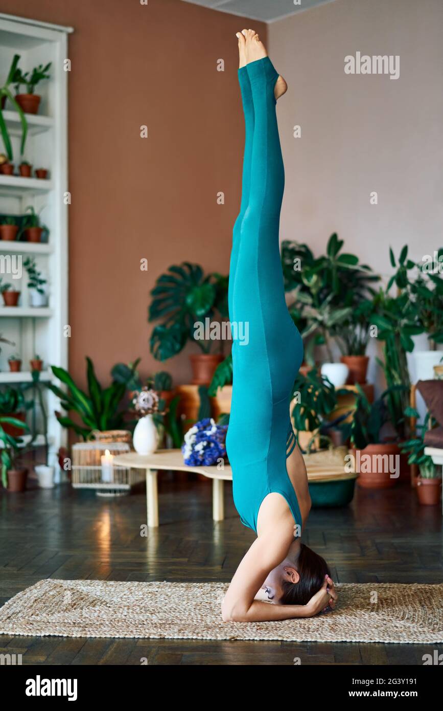 Junge schlanke Frau macht Yoga Asana unterstützt Kopfstand zu Hause Stockfoto