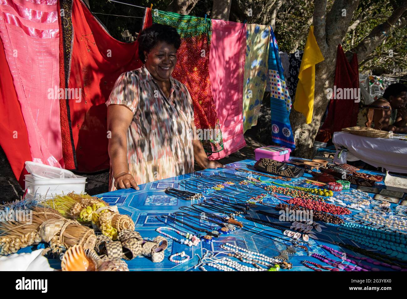 Lächelnde Frau mit Kunsthandwerk und Pareo-Handtüchern zum Verkauf an einem Souvenirstand am Strand, Sawa-i-Lau Island, Yasawa Group, Fidschi-Inseln, South Pacifi Stockfoto