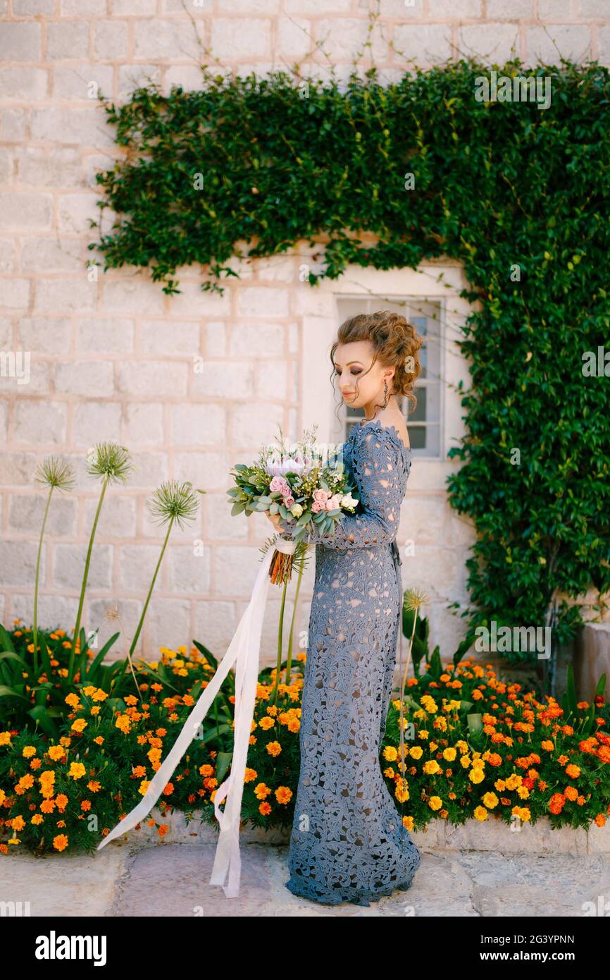Eine Braut in einem blauen Kleid mit einem Blumenstrauß steht an der Wand  eines Hauses mit einer grünen Liane und orangen Blumen, Nahaufnahme  Stockfotografie - Alamy
