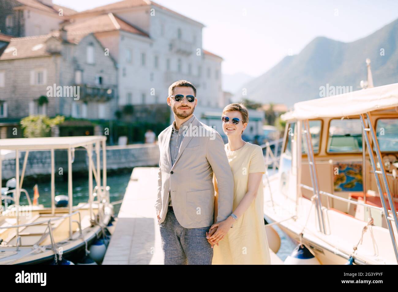 Ein Mann und eine Frau in Sonnenbrillen stehen umarmt Andere auf dem Pier in der Nähe der Touristenboote und halten Hände Stockfoto