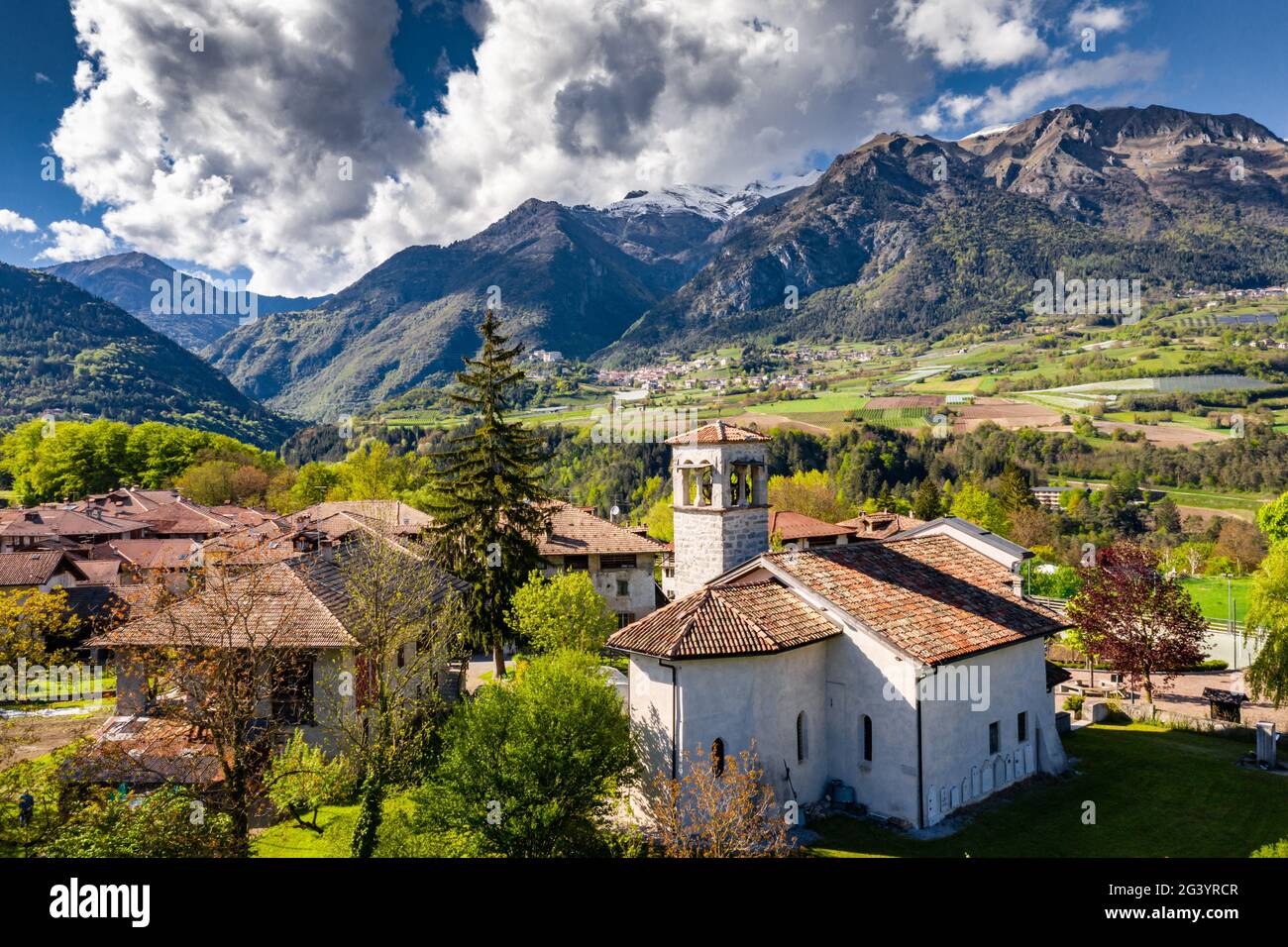 Luftaufnahme des Tales mit Kirche in Cares, Trentino, grüne Hänge der Berge Italiens, riesige Wolken über einem Tal, Dach zu Stockfoto