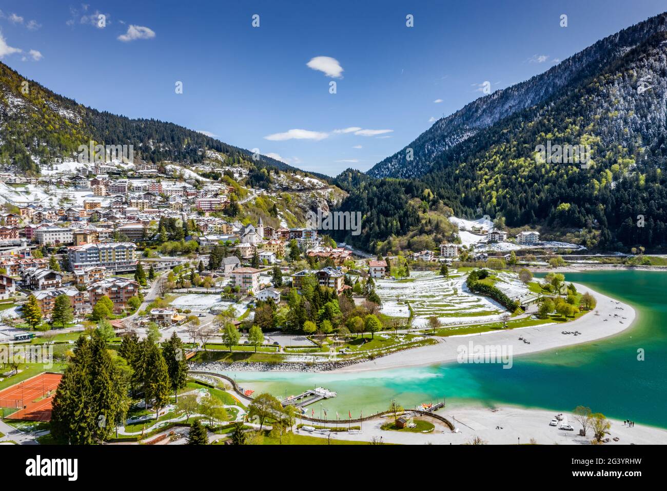 Die unwahrscheinliche Luftlandschaft des Dorfes Molveno, Italien, azurblaues Wasser des Sees, leerer Strand, schneebedeckte Berge Dolomiten auf Stockfoto