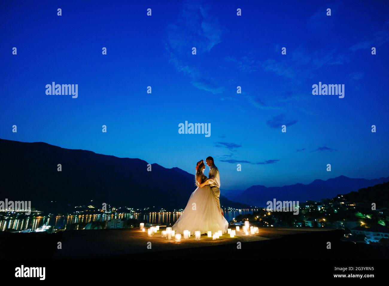 Die Braut und der Bräutigam umarmen sich bei Sonnenuntergang auf der Aussichtsplattform über der Altstadt von Kotor, hinter ihnen der Abendhafen in Lig Stockfoto