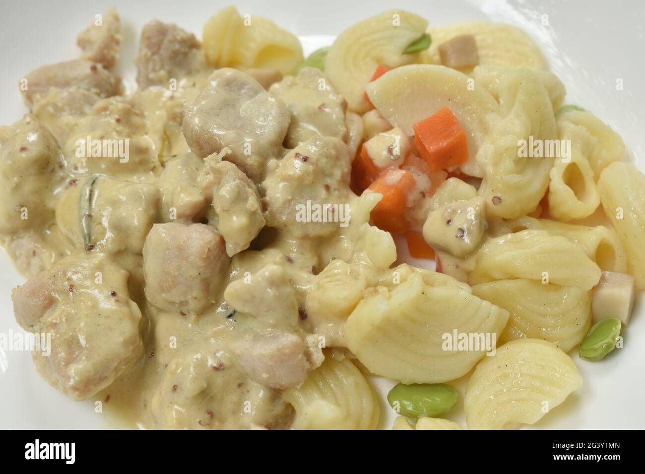 Gedünstetes Makkarodressing aus Schweinefleisch und Pilzen mit grüner Erbse in weißer Sahnesauce auf dem Teller Stockfoto