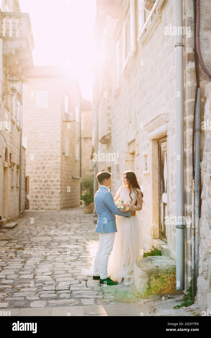 Die Braut und der Bräutigam umarmen sich in einer schönen alten Straße Von Perast in der Nähe einer weißen Steinmauer Stockfoto
