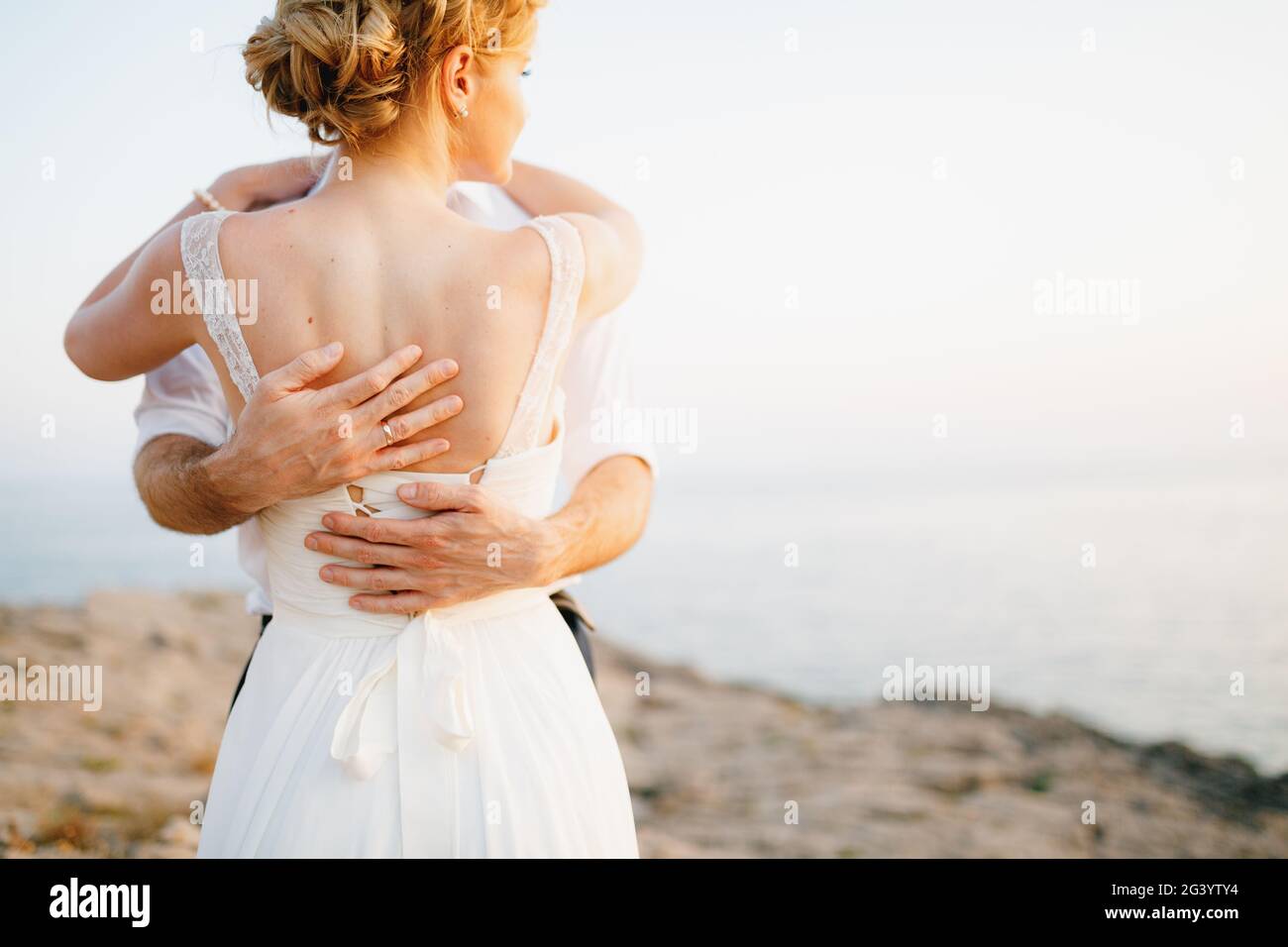 Die Braut und der Bräutigam umarmen sich auf den Felsen am Meer vor der Kulisse der Berge und der Insel Mamula, Rückansicht Stockfoto