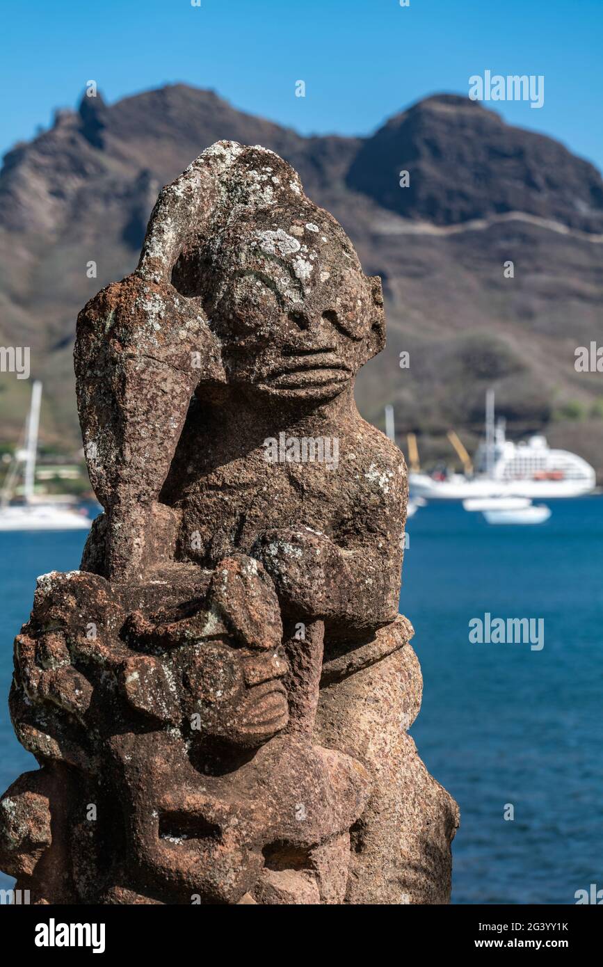 Detail einer Tiki-Statue mit dem Passagierfrachtschiff Aranui 5 (Aranui Cruises) auf dem Pier in der Ferne, Taiohae, Nuku Hiva, Marquesas-Inseln, French Pol Stockfoto