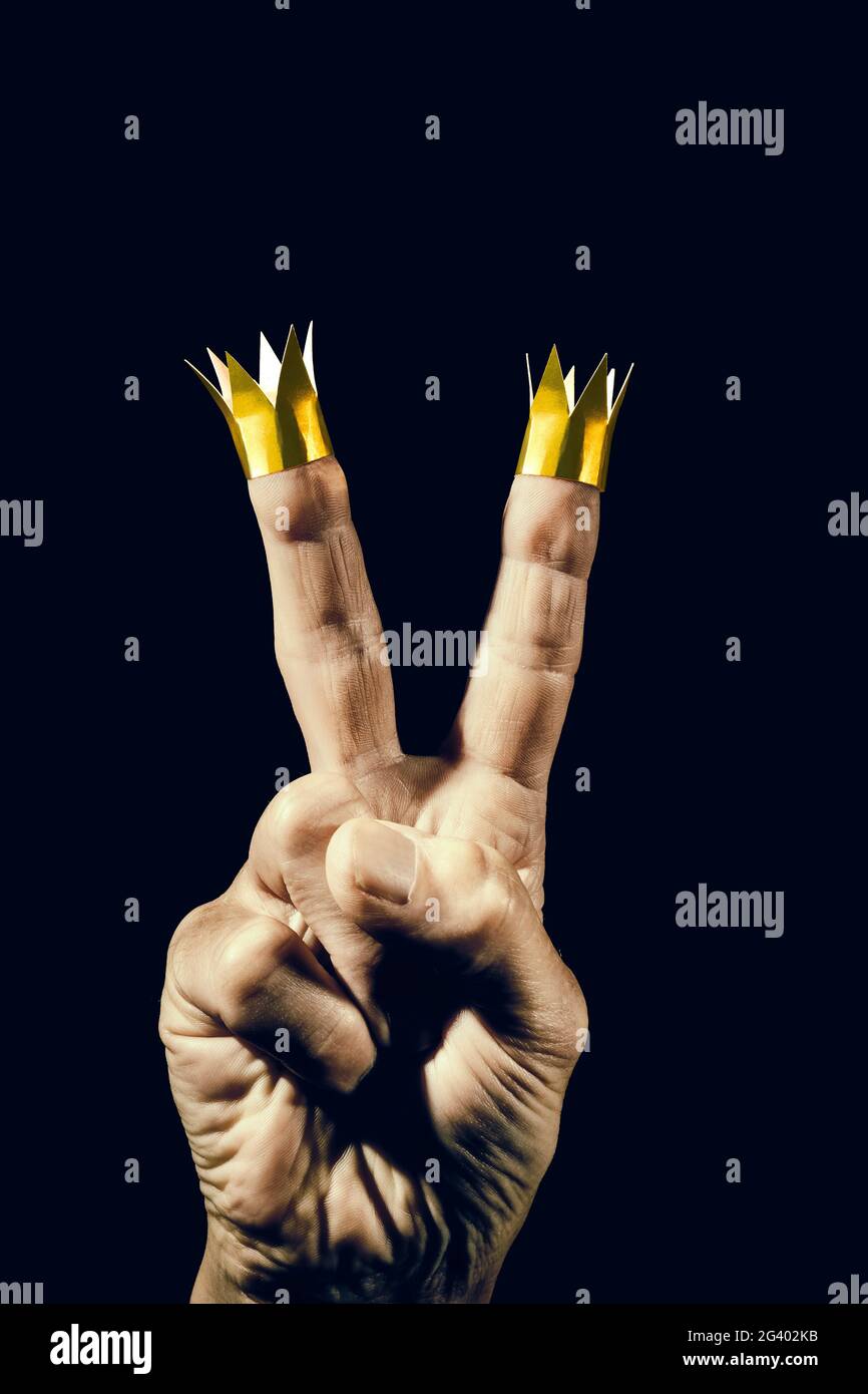 Hand macht ein Siegeszeichen mit Papierkronen auf den Fingern. Stockfoto
