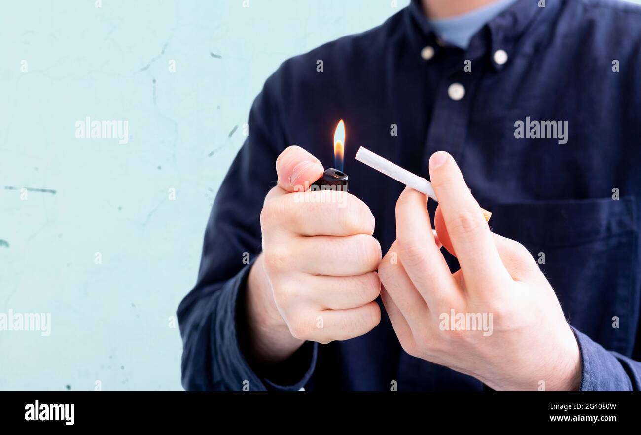 Person, die eine Feuerzeugflamme und eine Zigarette in der Hand hält, raucht einen schlechten Habbit Stockfoto