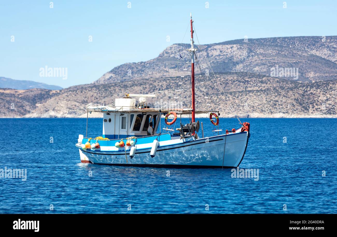 Fischerboot bunt am offenen Meer, iOS Insel Küste Hintergrund vertäut. Kykladen, Griechenland. Traditionelles altes Holzgefäß, das auf ruhigem Wasser verankert ist. Sunny d Stockfoto