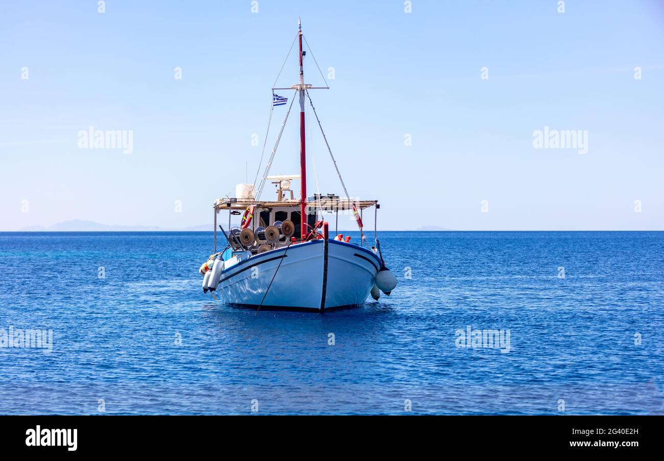 Fischerboot bunt am offenen Meer, iOS Insel Kykladen, Griechenland vertäut. Traditionelles altes Holzgefäß, das auf ruhigem Wasser verankert ist. Sonniger Tag, klarer blauer Himmel Stockfoto