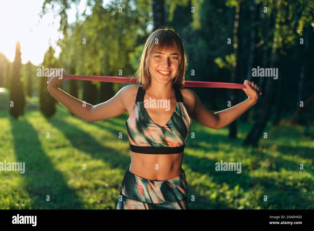 Glückliche junge Frau, die im Freien trainiert. Fitness Gummiband in den Händen eines lächelnden Mädchens. Stockfoto