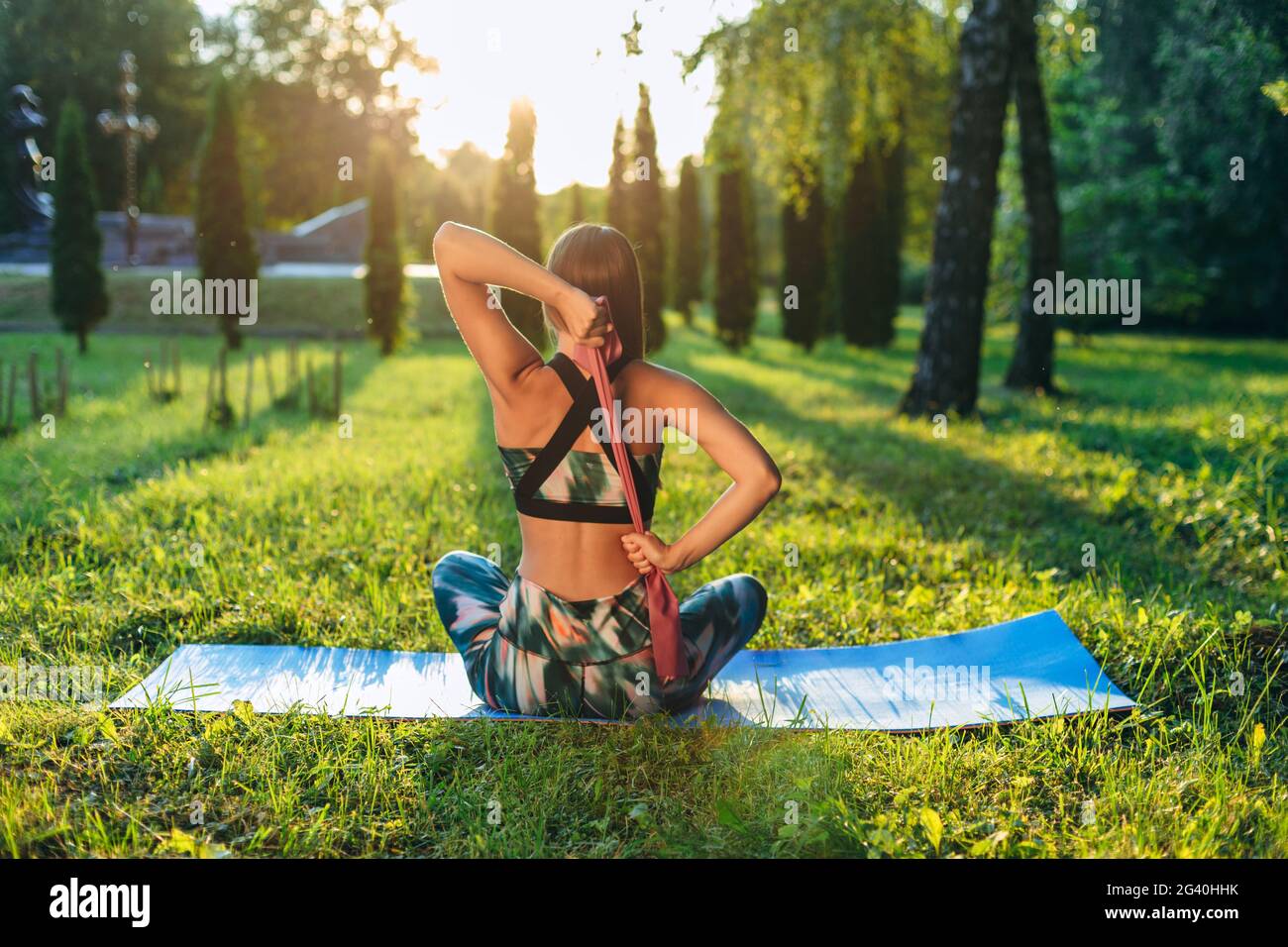 Das Konzept eines gesunden Lebensstils. Das Mädchen praktiziert Yoga auf einer Matte im Park. Fitness-Gummiband in den Händen eines jungen Athleten. Stockfoto