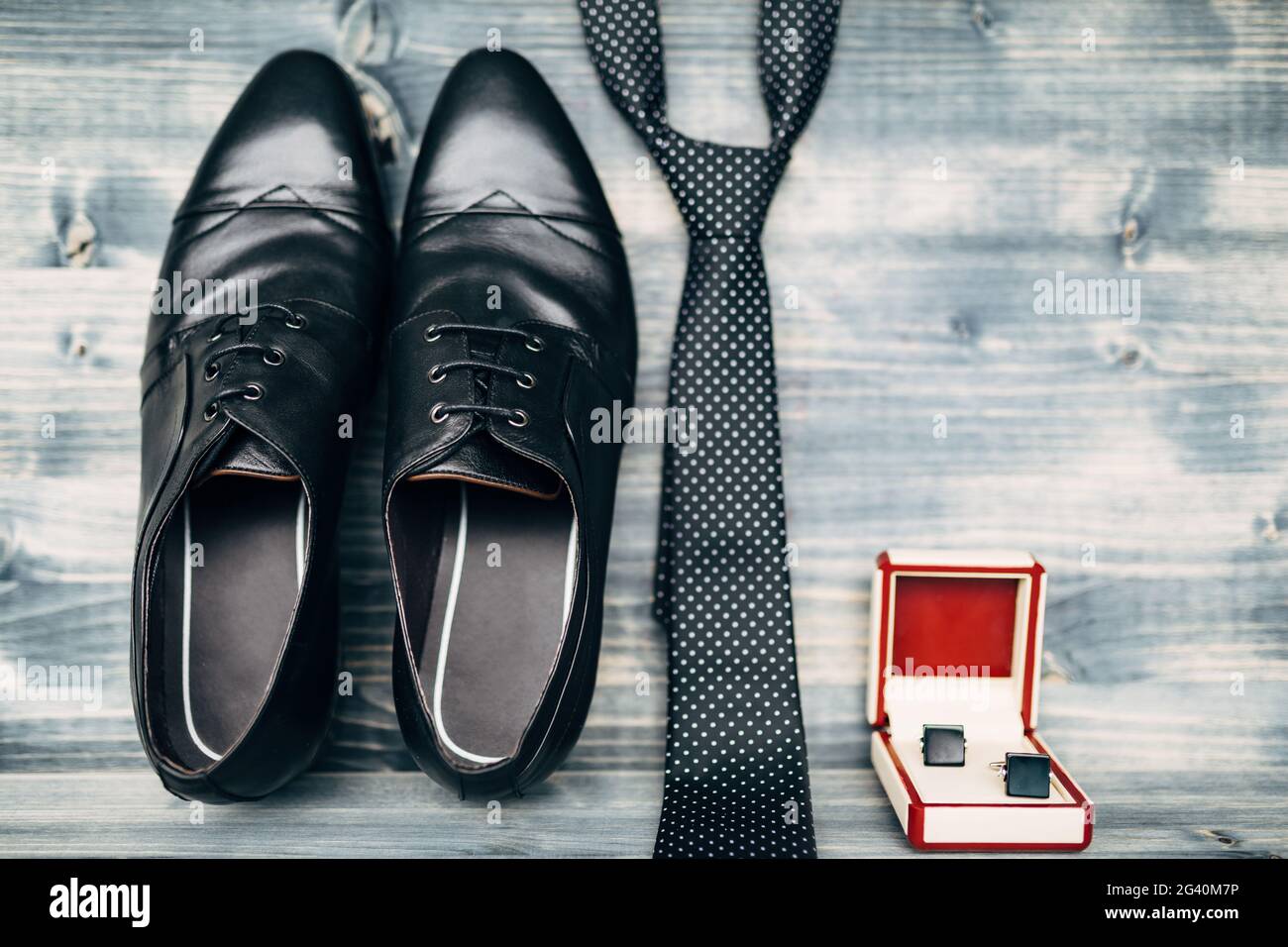Schwarze Leder Herrenschuhe mit Manschettenknöpfen in einer rot-weißen Box mit einer gepunkteten Krawatte auf einer Holzstruktur. Stockfoto