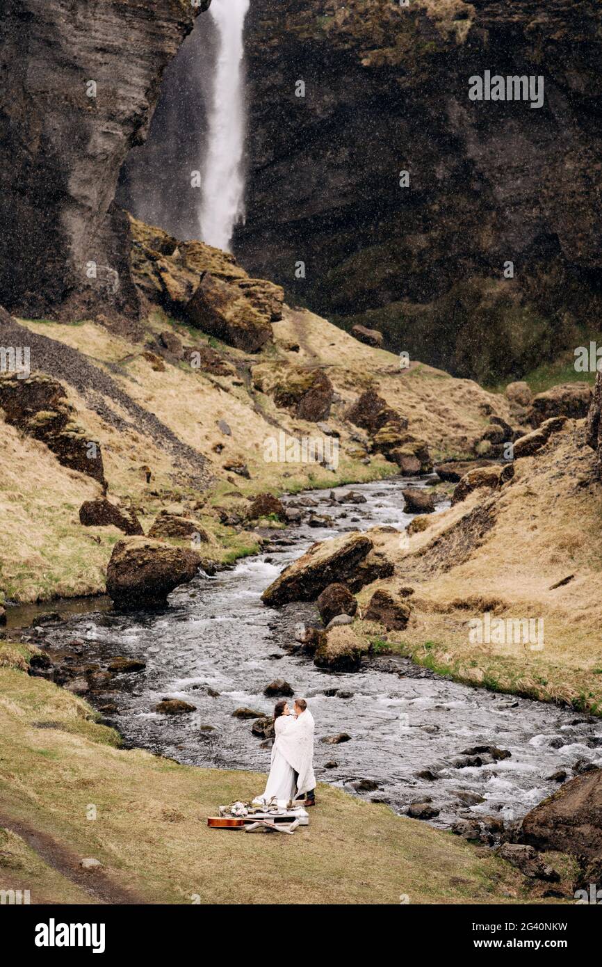 Reiseziel Island Hochzeit, in der Nähe des Kvernufoss Wasserfalls. Ein Brautpaar steht unter einem karierten Dach in der Nähe eines Bergflusses. Der Bräutigam h Stockfoto