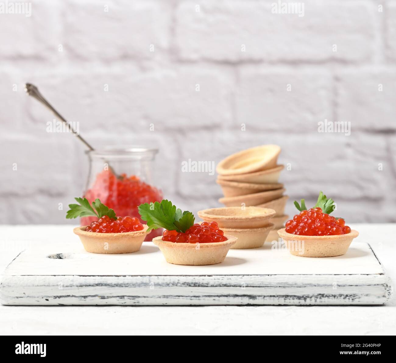 Roter Kaviar im Glasgefäß und runde Törtchen auf einem weißen Tisch Stockfoto