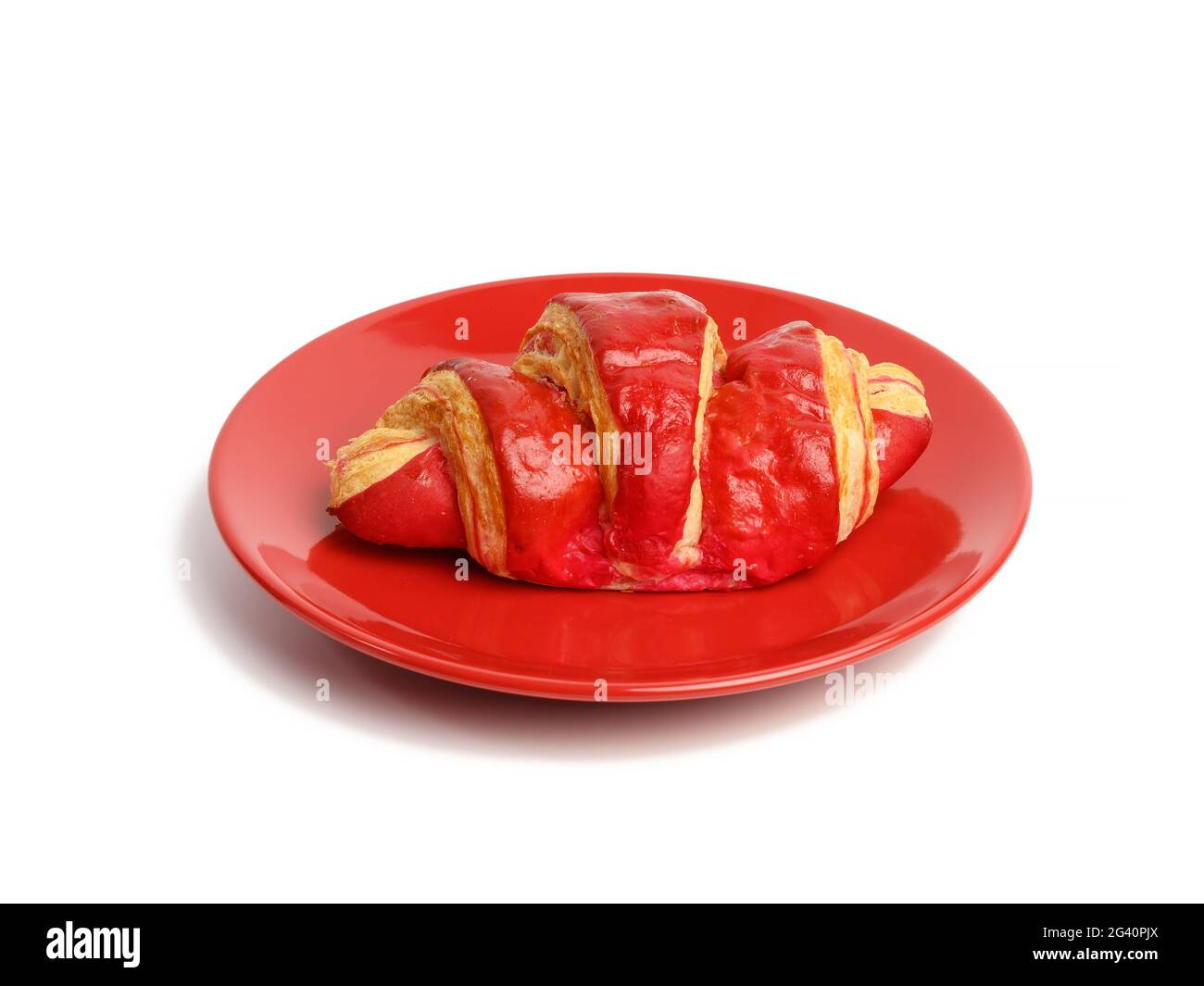 Gebackene Croissants mit Kirschglasur auf einer roten Keramikplatte, Stockfoto
