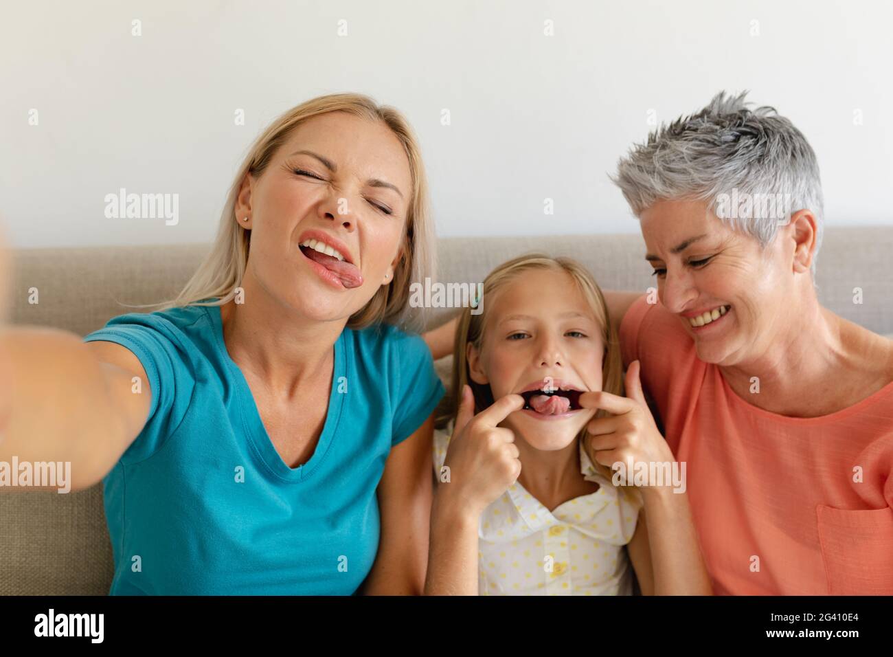 Kaukasische Mutter sitzt auf der Couch und macht Selfie mit Gesichtern Tochter und Großmutter Stockfoto