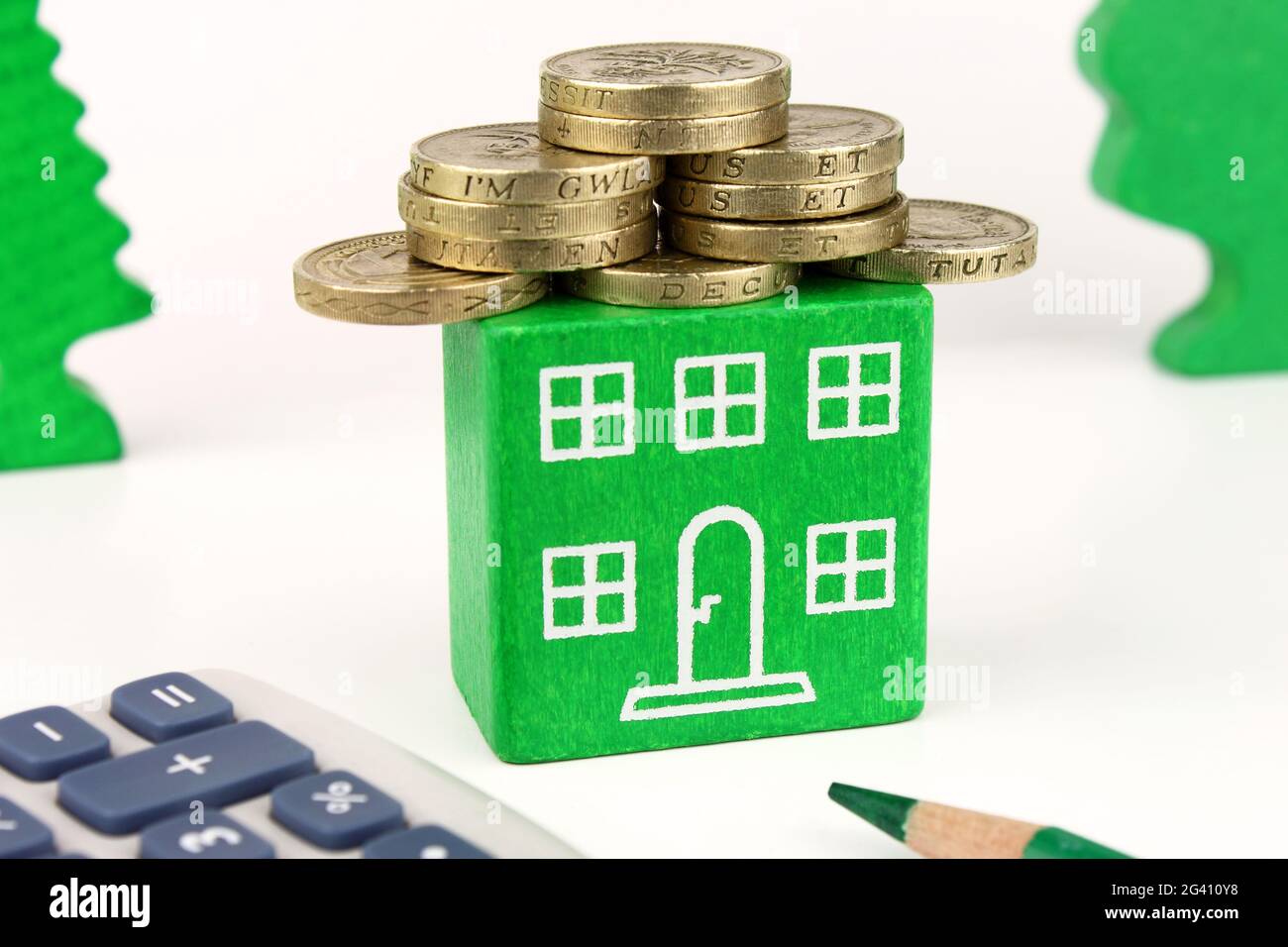 Ein grünes Haus mit Münzen für das Dach, was Einsparungen darstellt, die mit einem energieeffizienten Haus erzielt werden können. Stockfoto